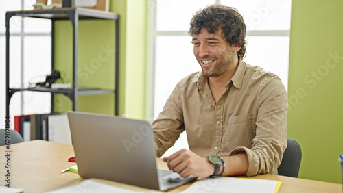 Young hispanic man business worker smiling confident sitting on table at office