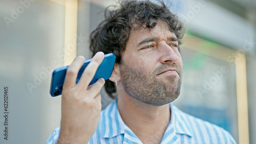 Young hispanic man listening to voice message at street