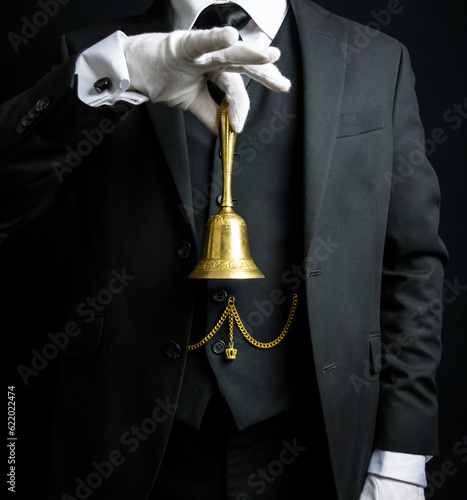 Portrait of Butler or Hotel Concierge in Dark Suit and White Gloves Holding Gold Bell. Concept of Ring for Service and Professional Hospitality.