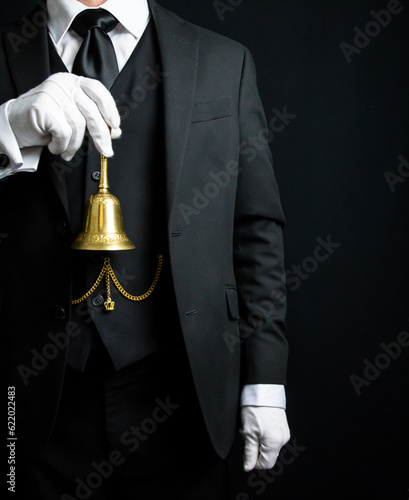 Portrait of Butler or Hotel Concierge in Dark Suit and White Gloves Holding a Gold Bell. Ring for Service Concept.