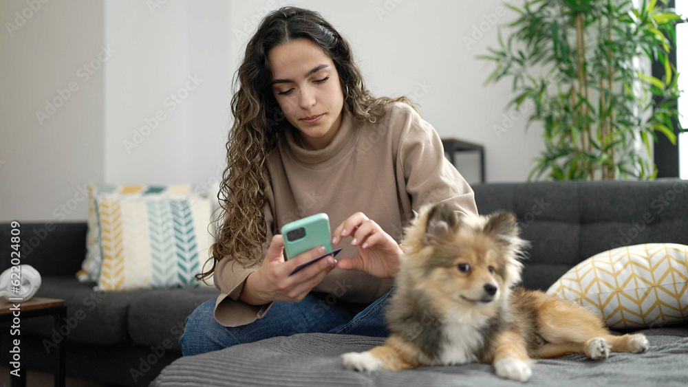 Young hispanic woman with dog shopping with smartphone and credit card sitting on sofa at home Young hispanic woman with dog shopping with smartphone and credit card sitting on sofa at home