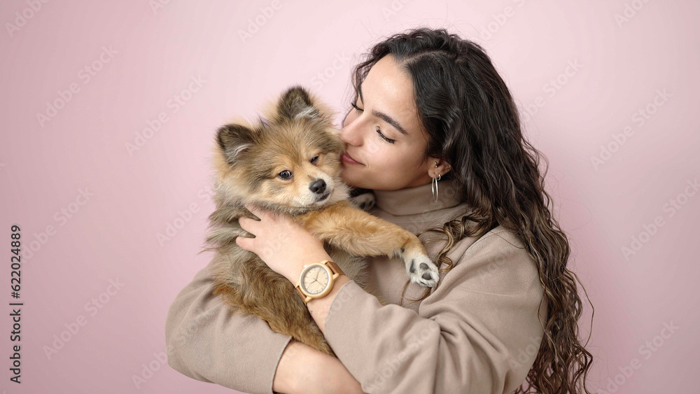 Young hispanic woman with dog smiling confident standing over isolated pink background