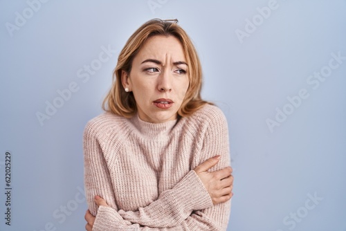 Foto Hispanic woman standing over blue background shaking and freezing for winter col