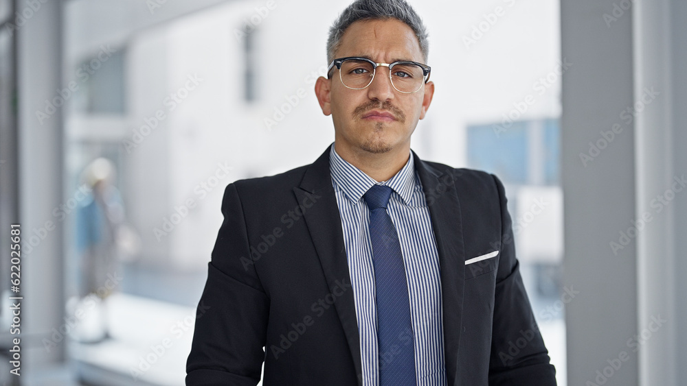 Young hispanic man business worker standing with serious face at office Young hispanic man business worker standing with serious face at office