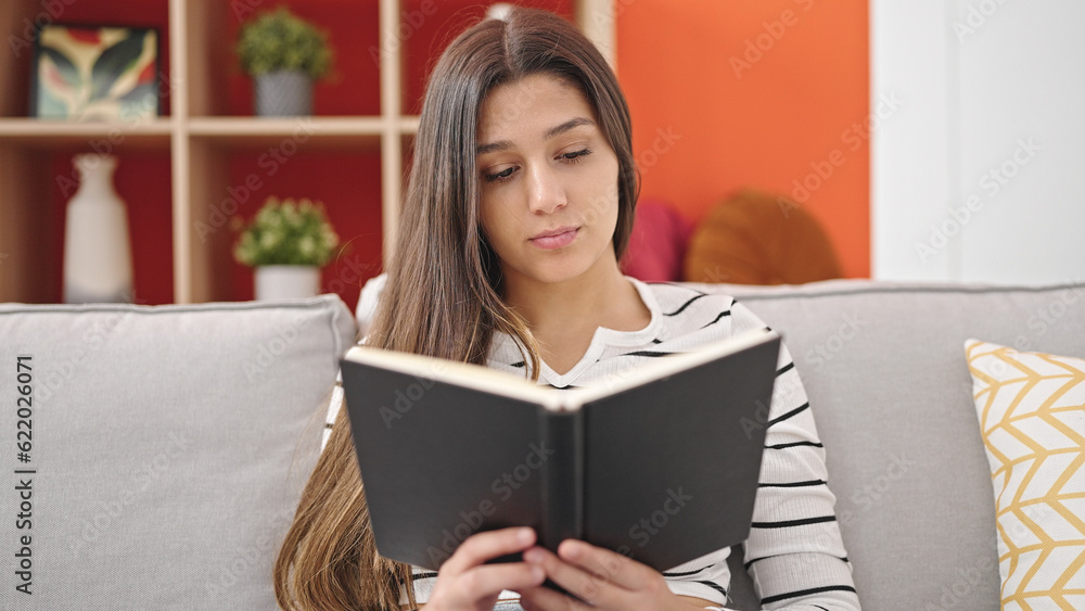 Young beautiful hispanic woman reading book sitting on sofa at home Young beautiful hispanic woman reading book sitting on sofa at home
