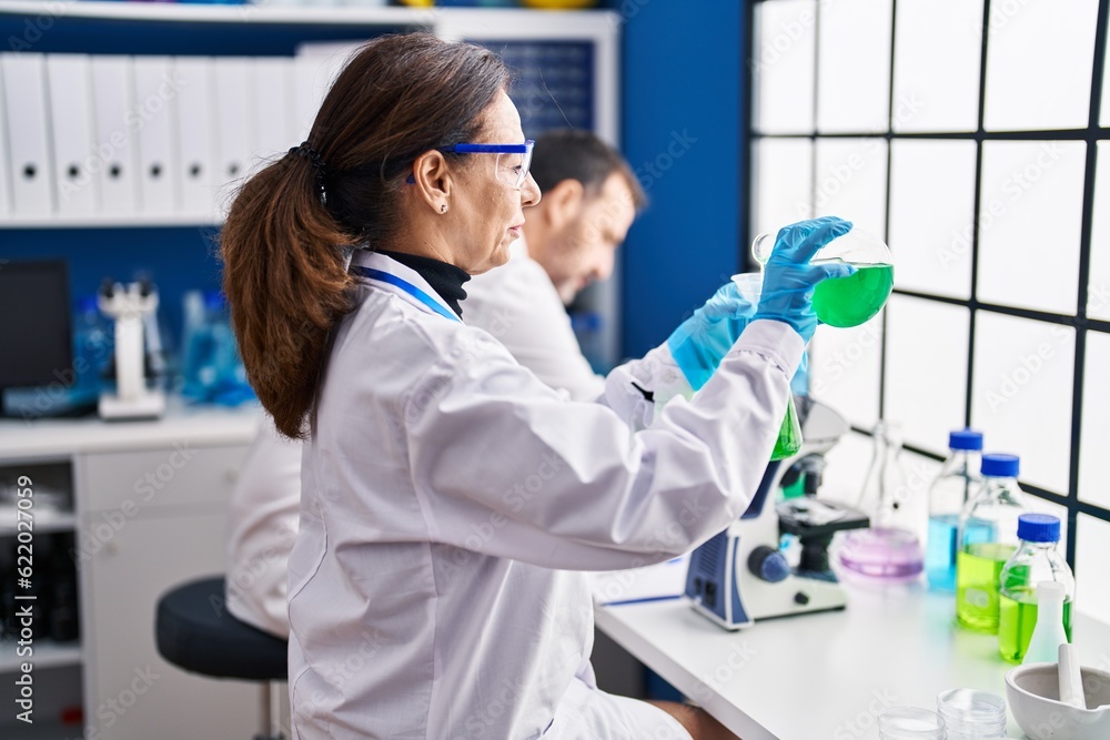 Middle age man and woman scientists measuring liquid at laboratory Middle age man and woman scientists measuring liquid at laboratory