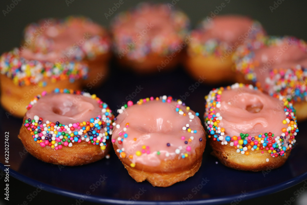 Donuts de creme cor-de-rosa cobertos com confetes coloridos, uma delícia irresistível na mesa de doces da festa infantil.