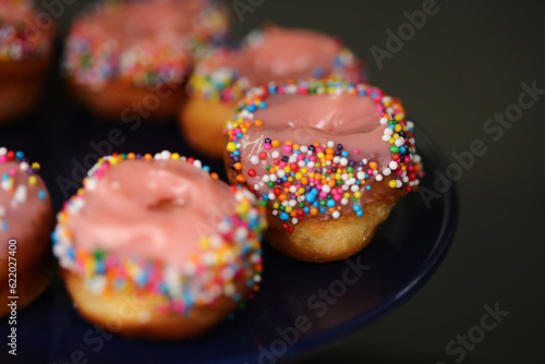 Donuts de creme cor-de-rosa cobertos com confetes coloridos, uma delícia irresistível na mesa de doces da festa infantil.