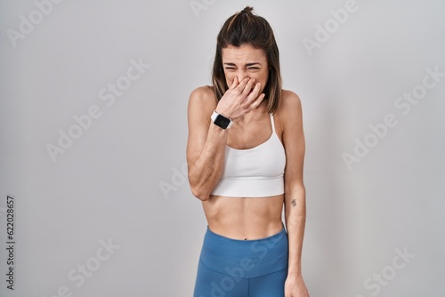 Hispanic woman wearing sportswear over isolated background smelling something stinky and disgusting, intolerable smell, holding breath with fingers on nose. bad smell © Krakenimages.com