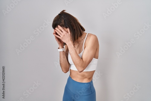 Hispanic woman wearing sportswear over isolated background with sad expression covering face with hands while crying. depression concept.