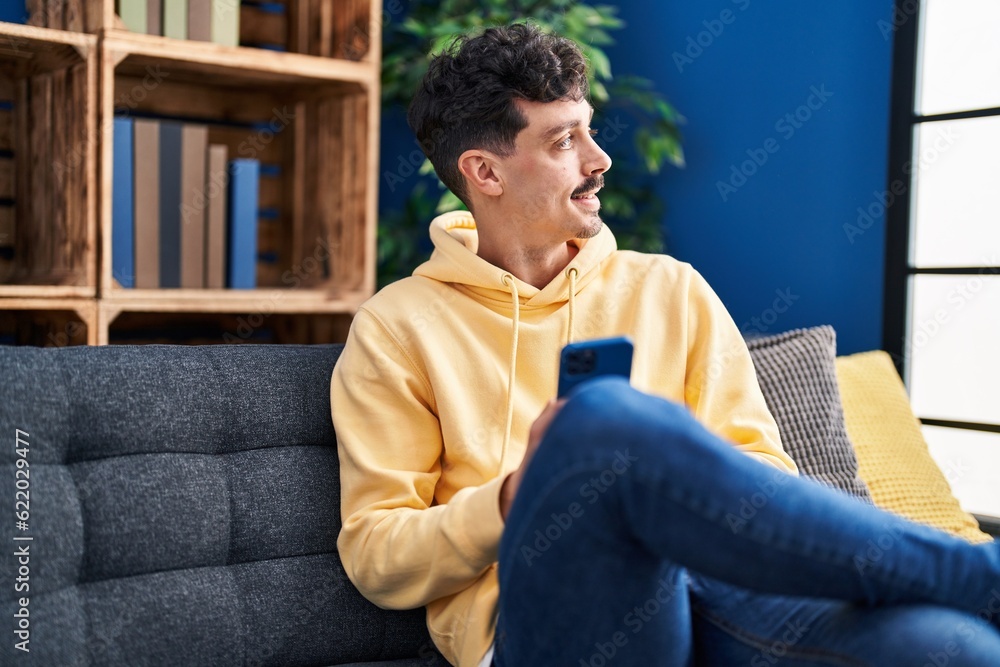 Young caucasian man using smartphone sitting on sofa at home