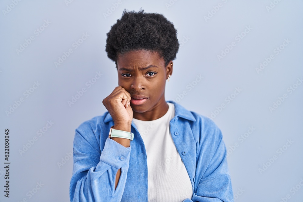 African american woman standing over blue background looking stressed and nervous with hands on mouth biting nails. anxiety problem. African american woman standing over blue background looking stressed and nervous with hands on mouth biting nails. anxiety problem.