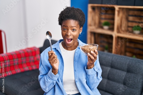 African american woman eating healthy whole grain cereals celebrating crazy and amazed for success with open eyes screaming excited.