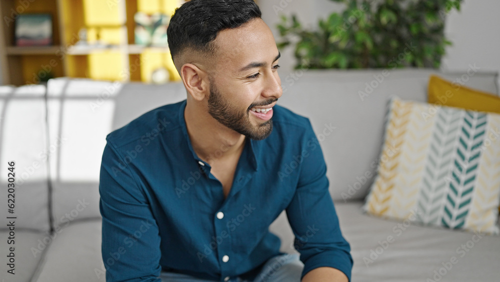 Obraz premium Young hispanic man smiling confident sitting on sofa at home