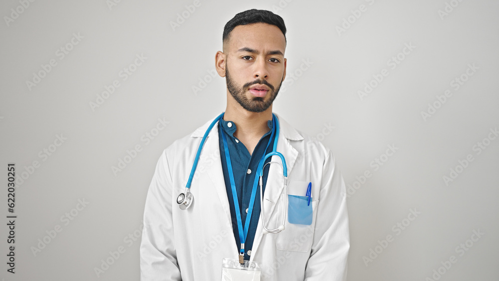 Young hispanic man doctor standing with serious expression over isolated white background Young hispanic man doctor standing with serious expression over isolated white background