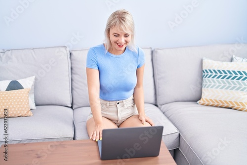 Young blonde woman watching movie on laptop at home