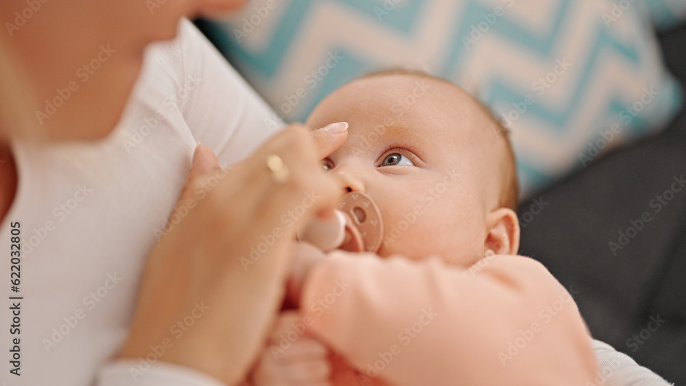 Mother and daughter sitting on sofa sucking pacifier at home Mother and daughter sitting on sofa sucking pacifier at home
