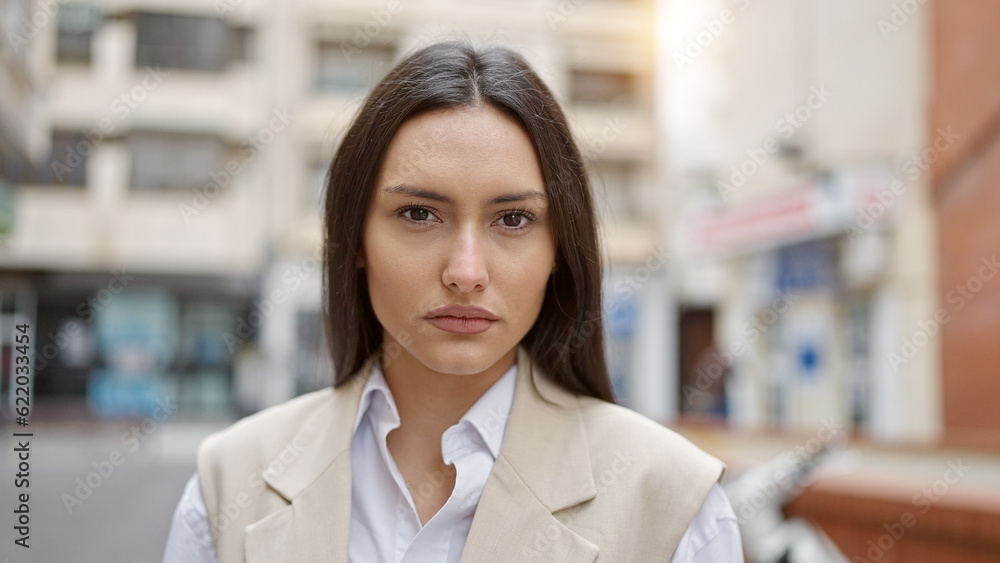 Young beautiful hispanic woman standing with serious expression at street