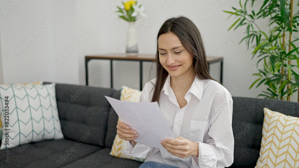 Young beautiful hispanic woman reading document sitting on sofa at home Young beautiful hispanic woman reading document sitting on sofa at home