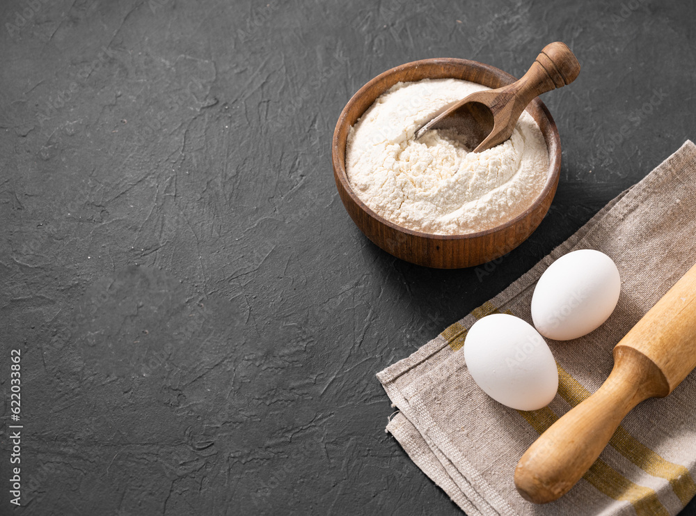 Organic baking ingredients. Flour, eggs and rolling pin on a dark background. Concept of homemade and healthy food. Organic baking ingredients. Flour, eggs and rolling pin on a dark background. Concept of homemade and healthy food.