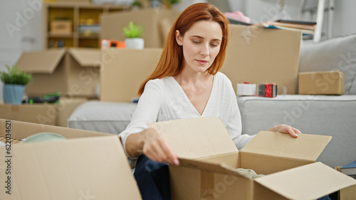 Young redhead woman sitting on floor unpacking at new home