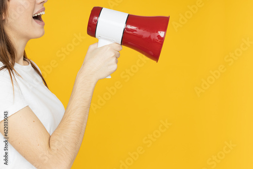 Woman talking into loudspeaker on yellow background, place for text
