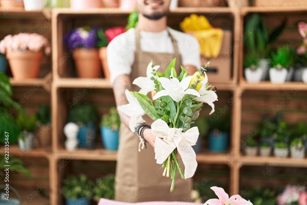 Young hispanic man florist holding bouquet of flowers at flower shop