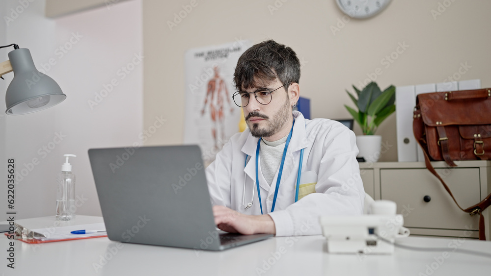 Fototapeta premium Young hispanic man doctor using laptop working at clinic