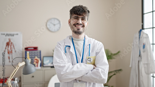 Young hispanic man doctor smiling confident standing with crossed arms at clinic