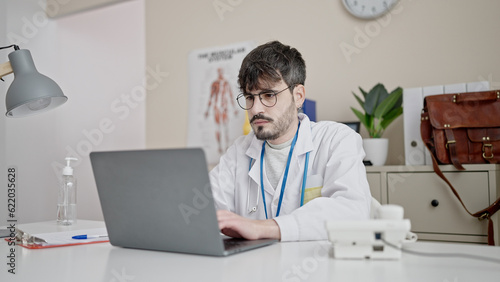 Young hispanic man doctor using laptop working at clinic