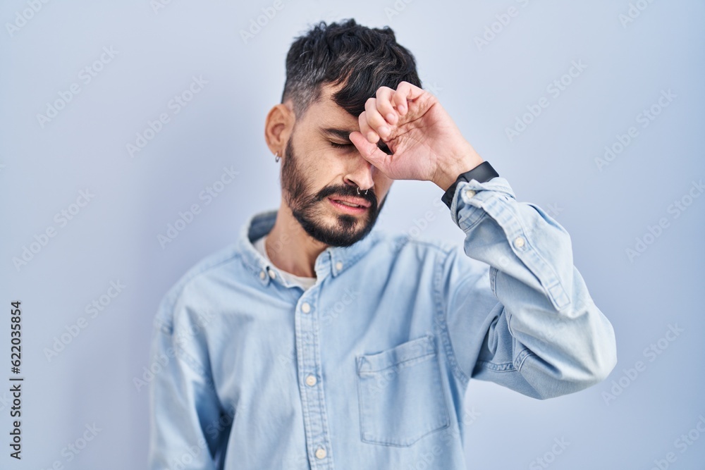 Young hispanic man with beard standing over blue background touching forehead for illness and fever, flu and cold, virus sick Young hispanic man with beard standing over blue background touching forehead for illness and fever, flu and cold, virus sick