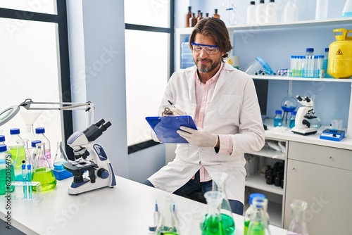 Middle age man scientist smiling confident writing on document at laboratory