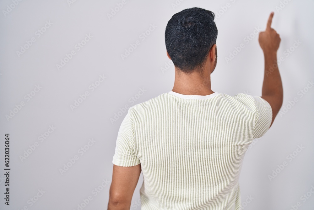 Hispanic man with beard standing over isolated background posing backwards pointing ahead with finger hand Hispanic man with beard standing over isolated background posing backwards pointing ahead with finger hand