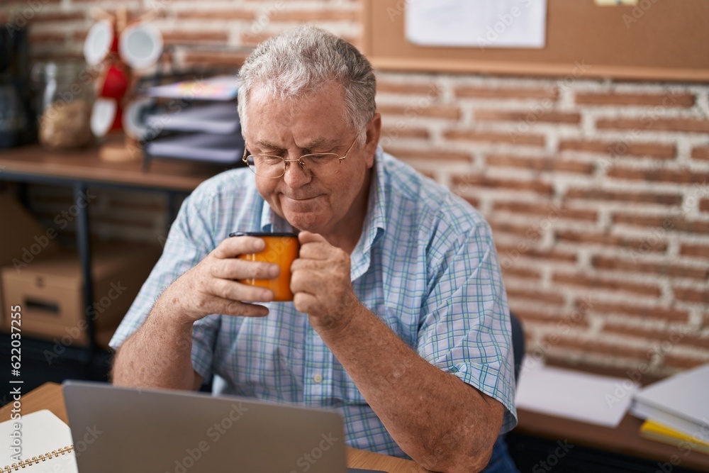 Middle age grey-haired man business worker using laptop drinking coffee at office Middle age grey-haired man business worker using laptop drinking coffee at office