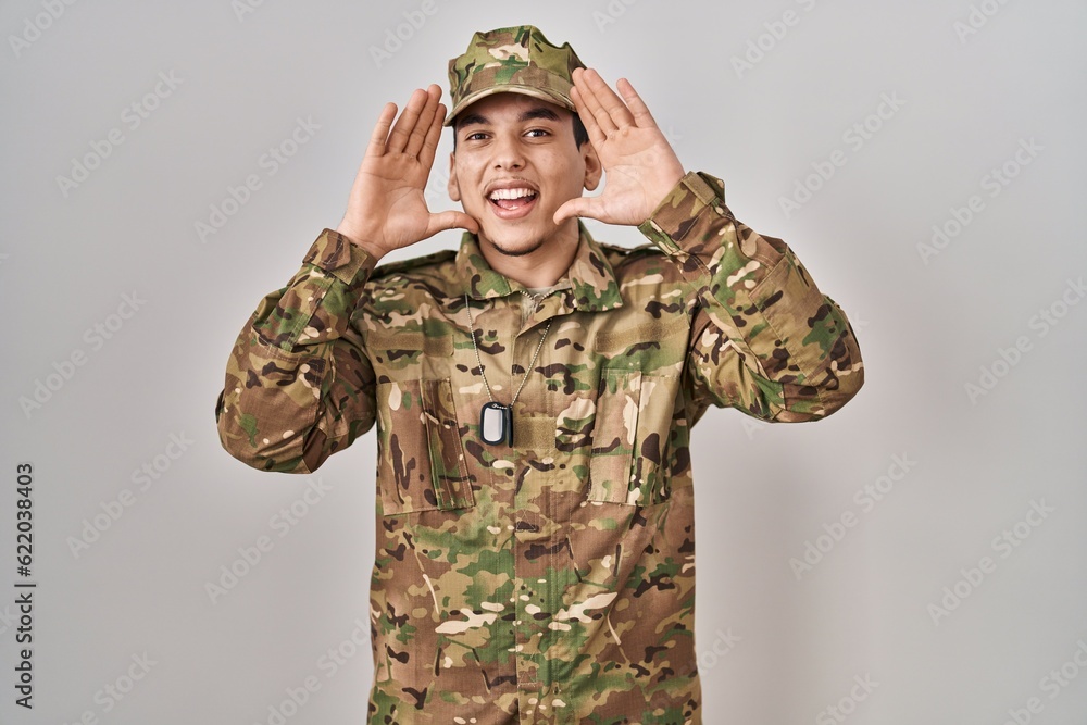 Young arab man wearing camouflage army uniform smiling cheerful playing peek a boo with hands showing face. surprised and exited Young arab man wearing camouflage army uniform smiling cheerful playing peek a boo with hands showing face. surprised and exited
