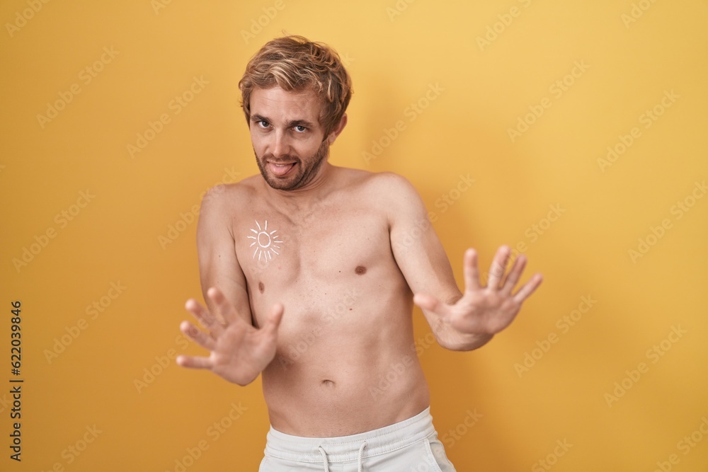 Caucasian man standing shirtless wearing sun screen afraid and terrified with fear expression stop gesture with hands, shouting in shock. panic concept.