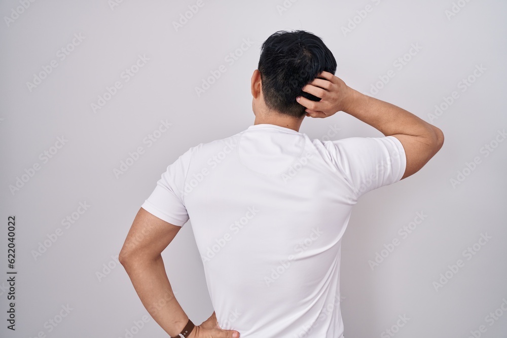 Young asian man standing over white background backwards thinking about doubt with hand on head Young asian man standing over white background backwards thinking about doubt with hand on head