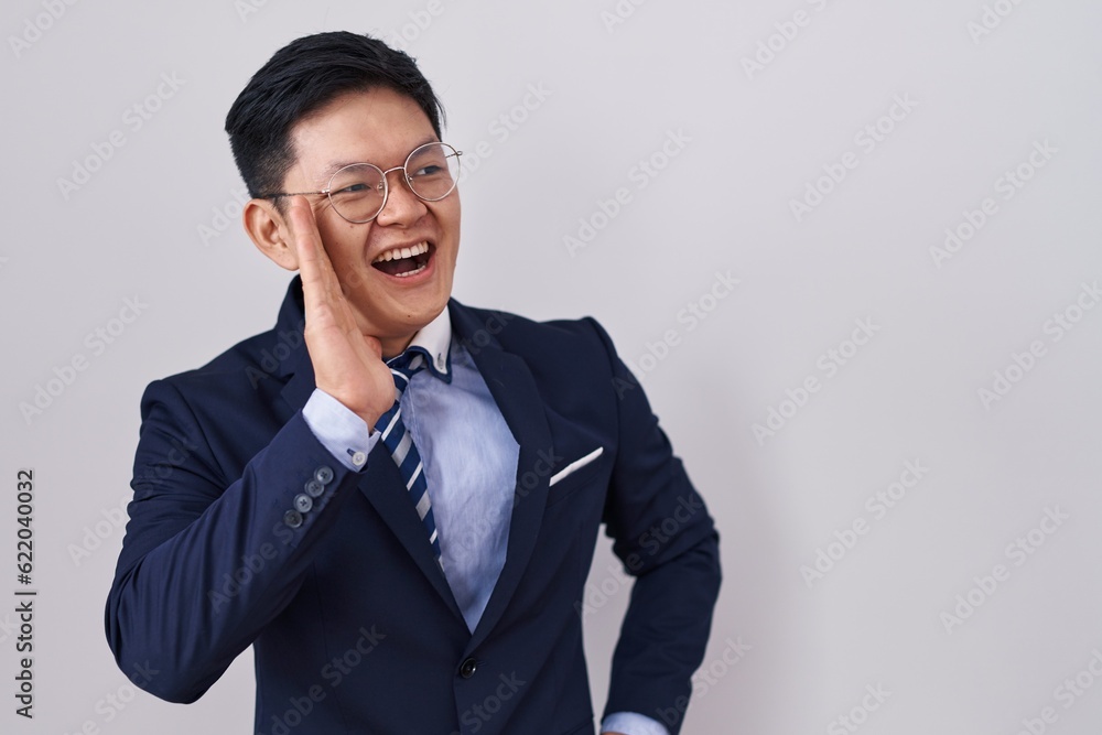Young asian man wearing business suit and tie shouting and screaming loud to side with hand on mouth. communication concept. Young asian man wearing business suit and tie shouting and screaming loud to side with hand on mouth. communication concept.
