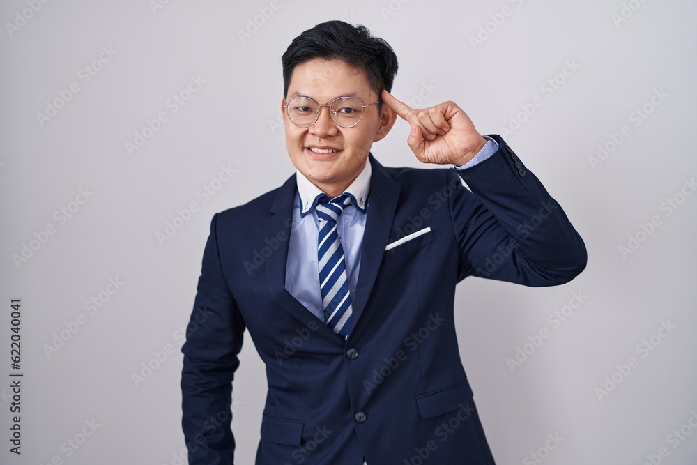 Young asian man wearing business suit and tie smiling pointing to head with one finger, great idea or thought, good memory Young asian man wearing business suit and tie smiling pointing to head with one finger, great idea or thought, good memory