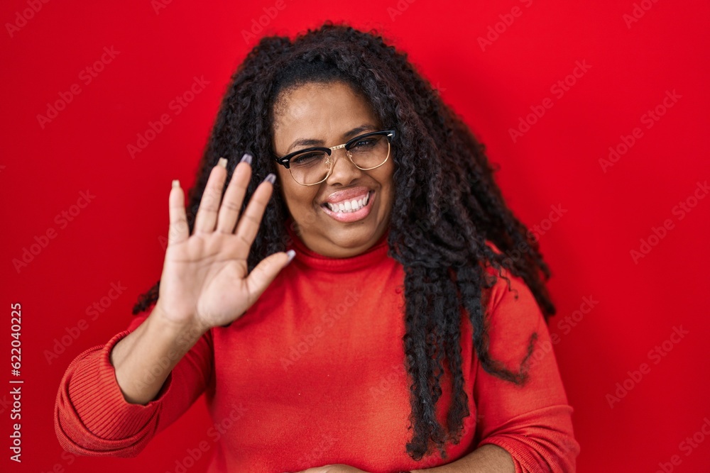 Plus size hispanic woman standing over red background waiving saying hello happy and smiling, friendly welcome gesture Plus size hispanic woman standing over red background waiving saying hello happy and smiling, friendly welcome gesture