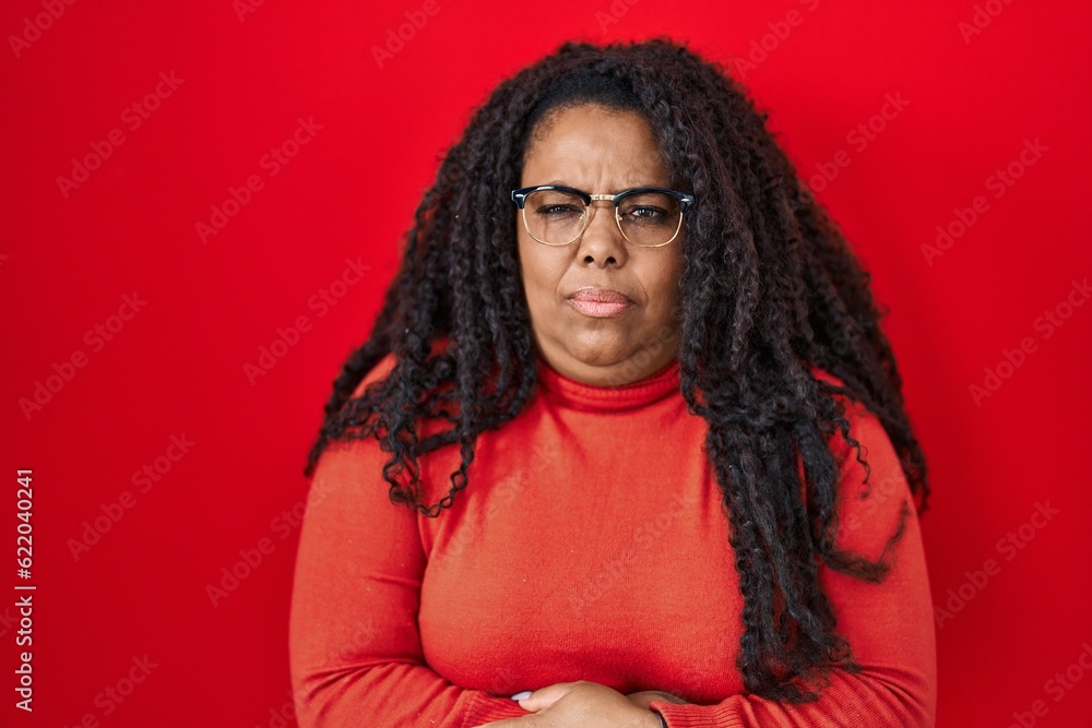 Plus size hispanic woman standing over red background with hand on stomach because indigestion, painful illness feeling unwell. ache concept. Plus size hispanic woman standing over red background with hand on stomach because indigestion, painful illness feeling unwell. ache concept.