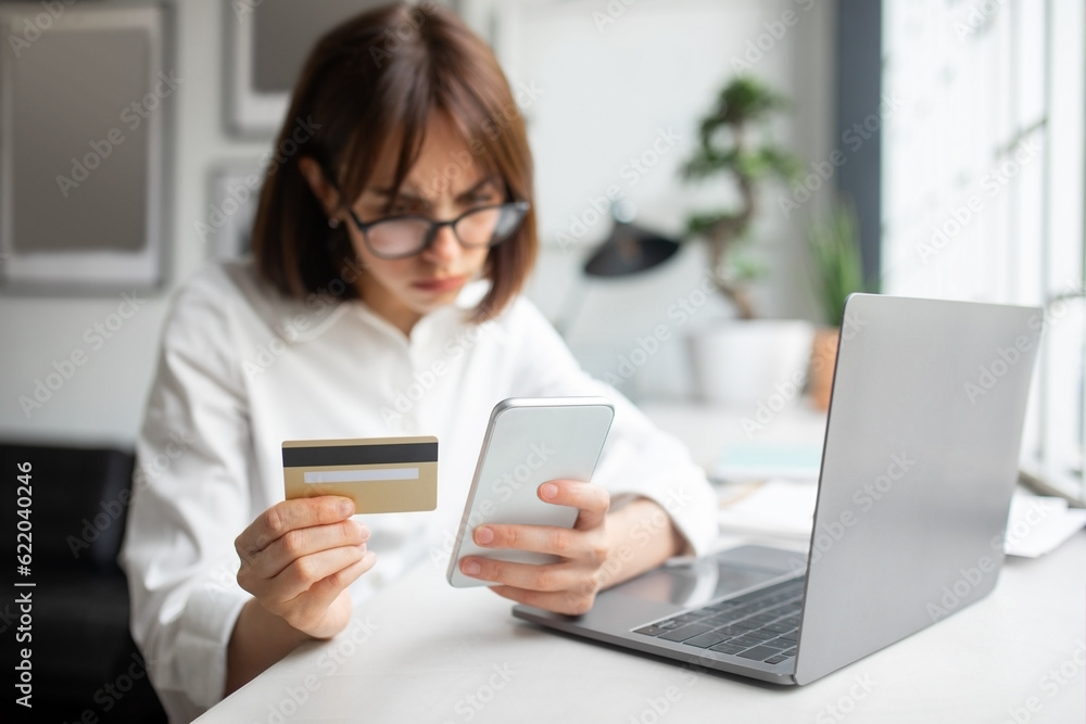 Problems with money banking app. Concentrated european young businesswoman using smartphone and credit card in office Problems with money banking app. Concentrated european young businesswoman using smartphone and credit card in office