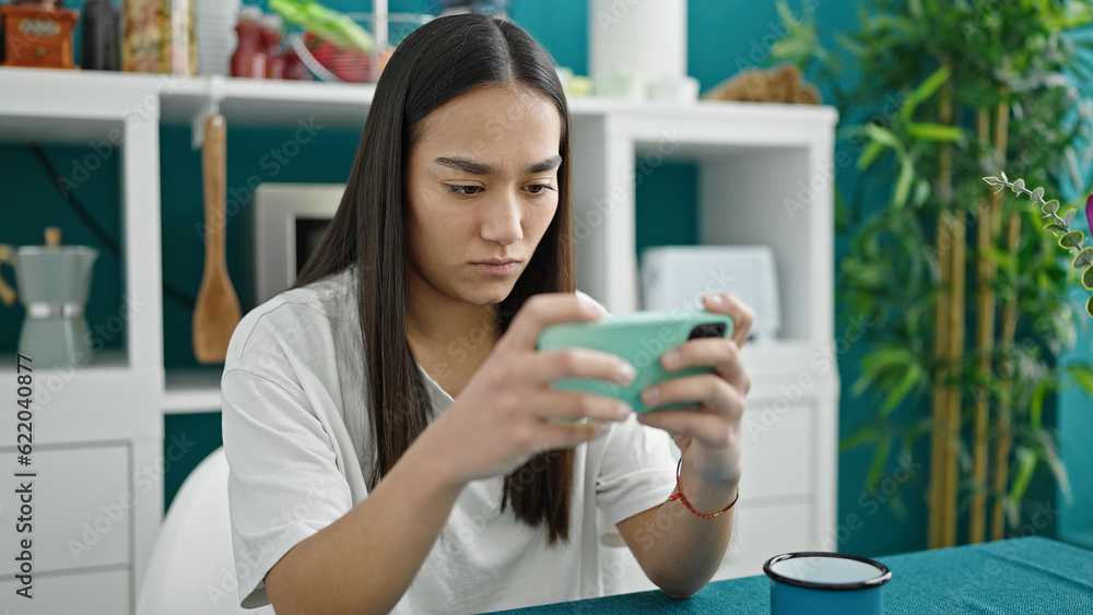 Young beautiful hispanic woman playing video game by smartphone at dinning room Young beautiful hispanic woman playing video game by smartphone at dinning room