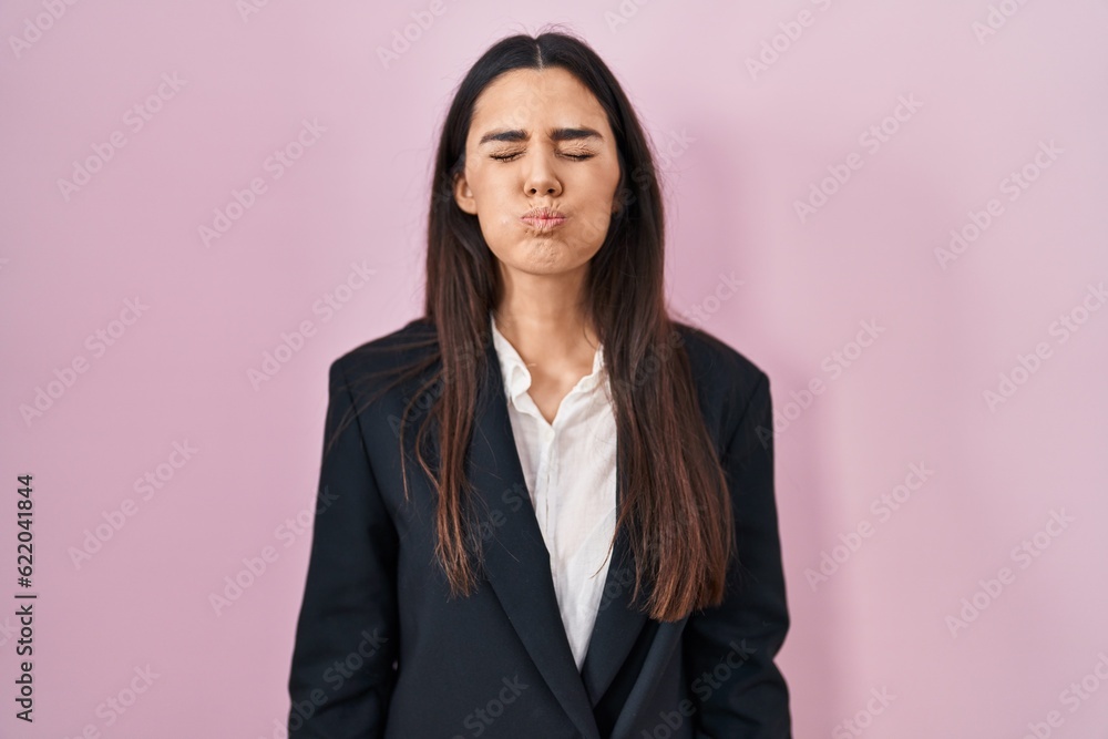 Young brunette woman wearing business style over pink background puffing cheeks with funny face. mouth inflated with air, crazy expression. Young brunette woman wearing business style over pink background puffing cheeks with funny face. mouth inflated with air, crazy expression.