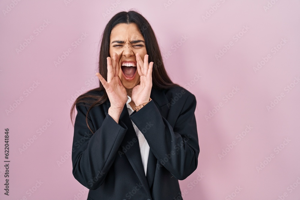 Young brunette woman wearing business style over pink background shouting angry out loud with hands over mouth Young brunette woman wearing business style over pink background shouting angry out loud with hands over mouth