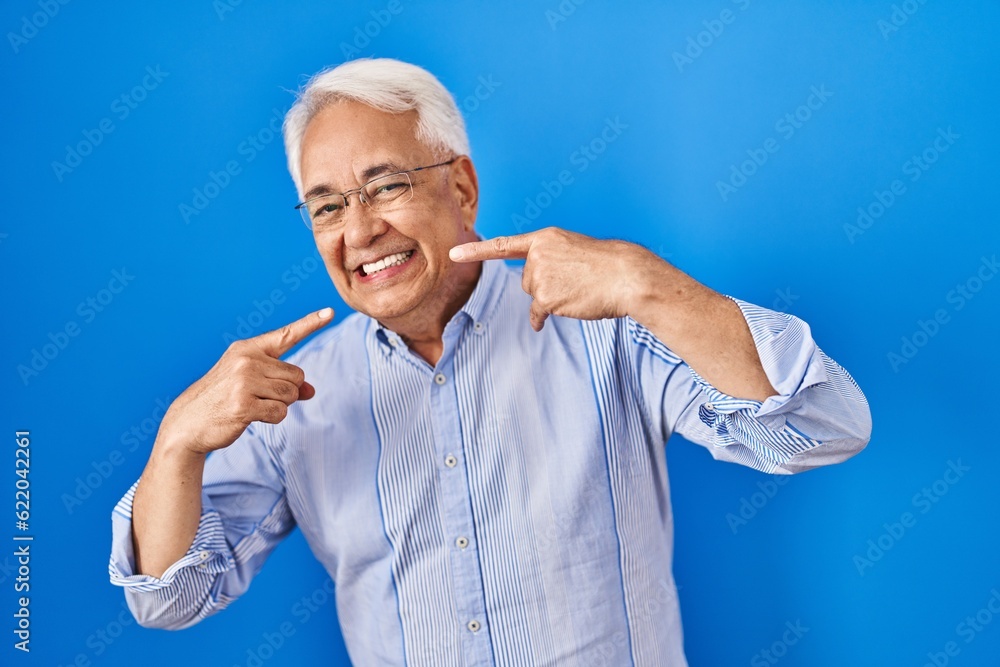 Hispanic senior man wearing glasses smiling cheerful showing and pointing with fingers teeth and mouth. dental health concept. Hispanic senior man wearing glasses smiling cheerful showing and pointing with fingers teeth and mouth. dental health concept.