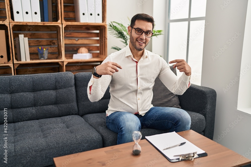 Young hispanic man with beard working at consultation office looking confident with smile on face, pointing oneself with fingers proud and happy. Young hispanic man with beard working at consultation office looking confident with smile on face, pointing oneself with fingers proud and happy.