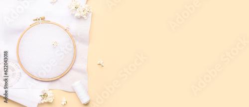 Wooden embroidery hoop with canvases, threads, pins and lilac flowers on beige background with space for text