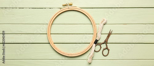 Wooden embroidery hoop with threads and scissors on green wooden background