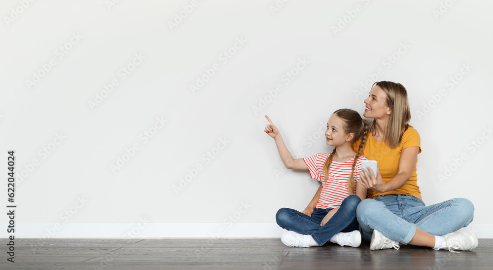 Mother And Little Daughter Relaxing With Smartphone And Pointing At Copy Space Mother And Little Daughter Relaxing With Smartphone And Pointing At Copy Space